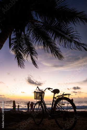 Bicycle on the beach near palm trees and ocean at sunset