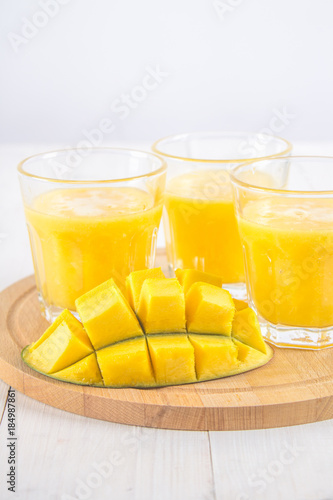 Yellow smoothie of mango, banana and orange on a white wooden table.