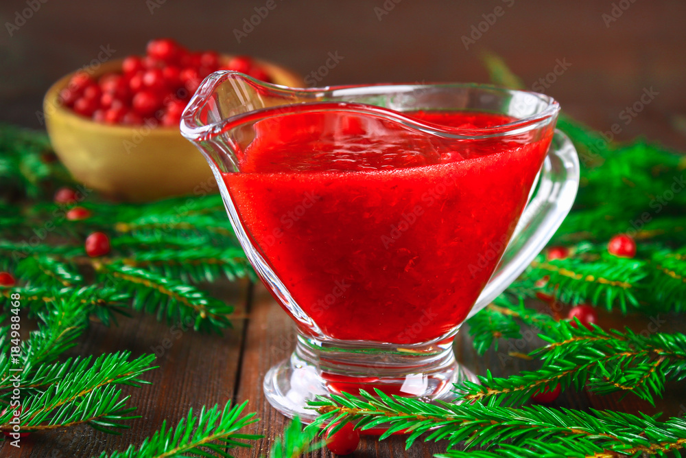 Cowberry cranberry sauce in a glass clear saucer on a wooden table with spruce branches. Cowberry cranberry sauce in a glass clear saucer on a wooden table with spruce branches.