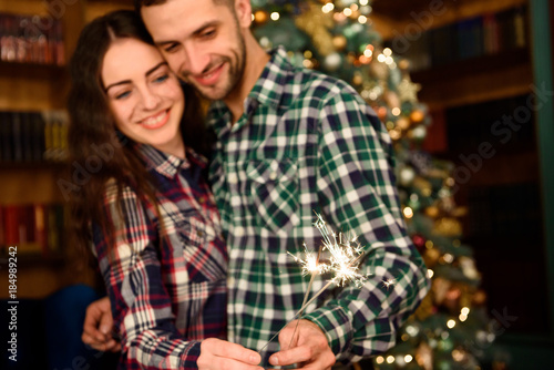 Sparklers and a kiss for Christmas! Young beautiful kisser and burning sparklers. Loving couple in Christmas decorated room.