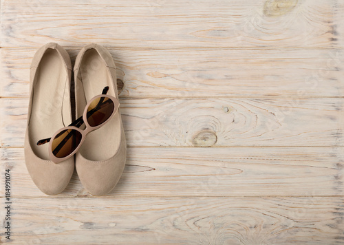 Women's shoes and sun glasses beige color on a wooden background.