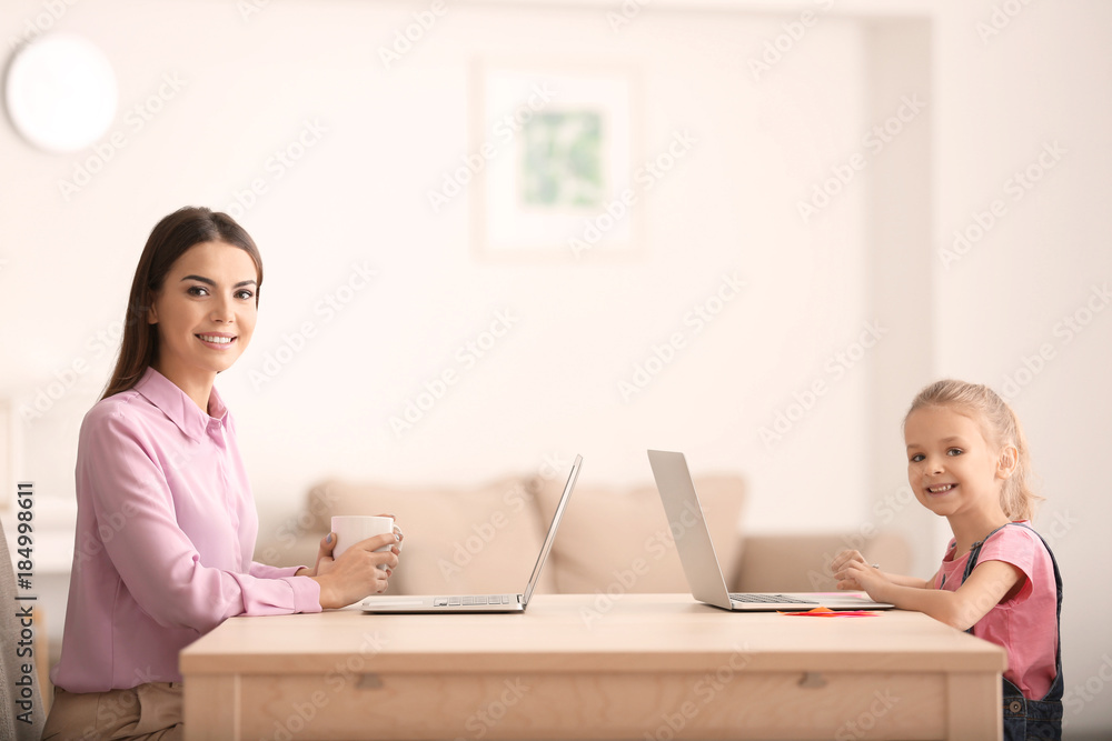 Young woman and her daughter with laptops at home