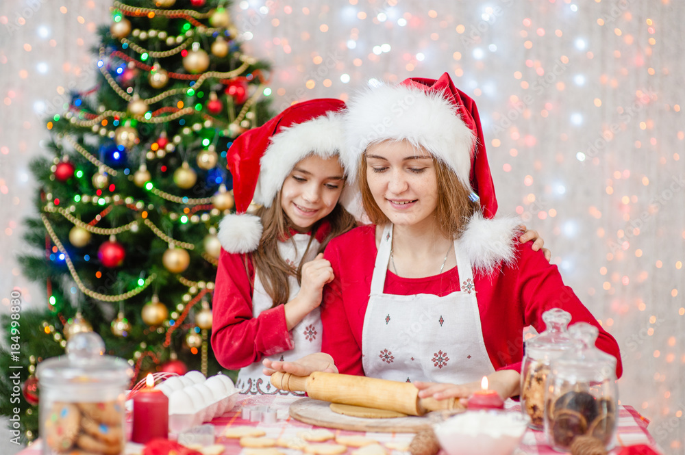 Mom and daughter in a Christmas hat prepare festive cookies at home Mom and daughter in a Christmas hat prepare festive cookies at home