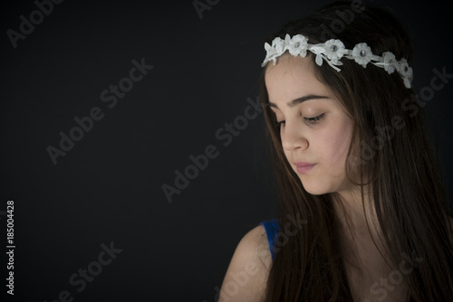 Portrait of Nice Little Girl 12 Y with Flower Crown Looking Down. Black Background. 