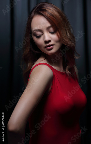 Charming brunette in a red dress posing on a black background.