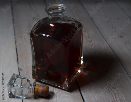 Whiskey/Rom/liquor in a vintage bottle being lidt from the side - casting colored light and shadows on wooden floor   boards