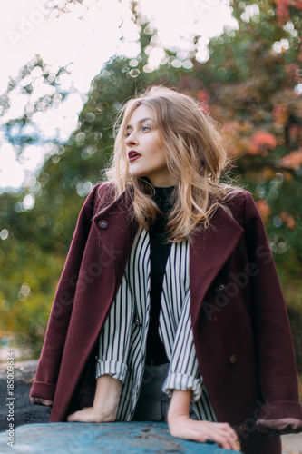 portrait of a luxurious, beautiful, young girl. Dressed in stylish clothes, walking in an autumn park. Bright lipstick on the lips.