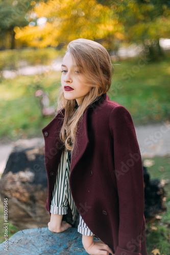 portrait of a luxurious, beautiful, young girl. Dressed in stylish clothes, walking in an autumn park. Bright lipstick on the lips.