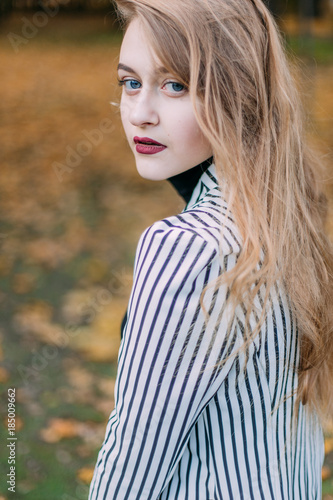 portrait of a luxurious, beautiful, young girl. Dressed in stylish clothes, walking in an autumn park. Bright lipstick on the lips.