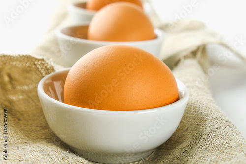 Raw brown chicken eggs in glass bowls on a white wooden table. Ingredients for cooking.
