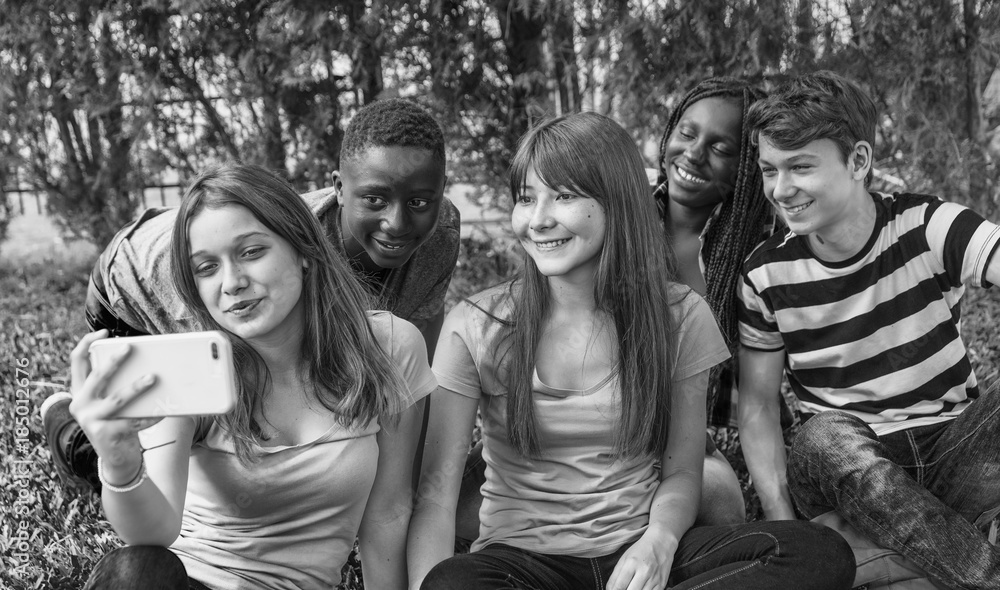 Fotografie Group of mixed races teenagers palying with smarthphone on the g