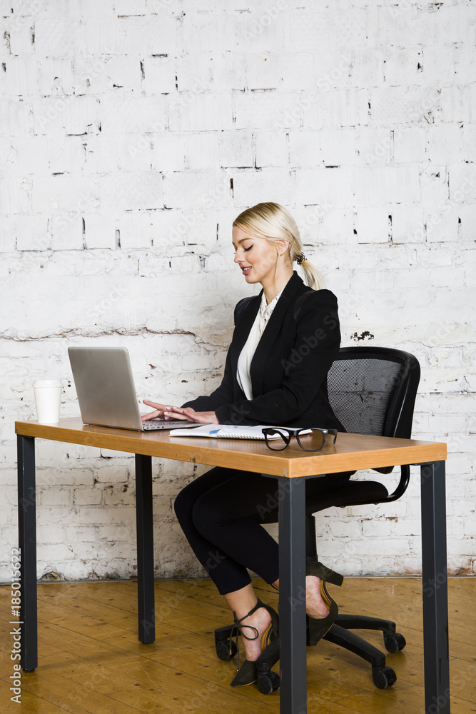 Φωτογραφία Young blond beauty businesswoman sitting at a office table with laptop, notebook and glasses in suit