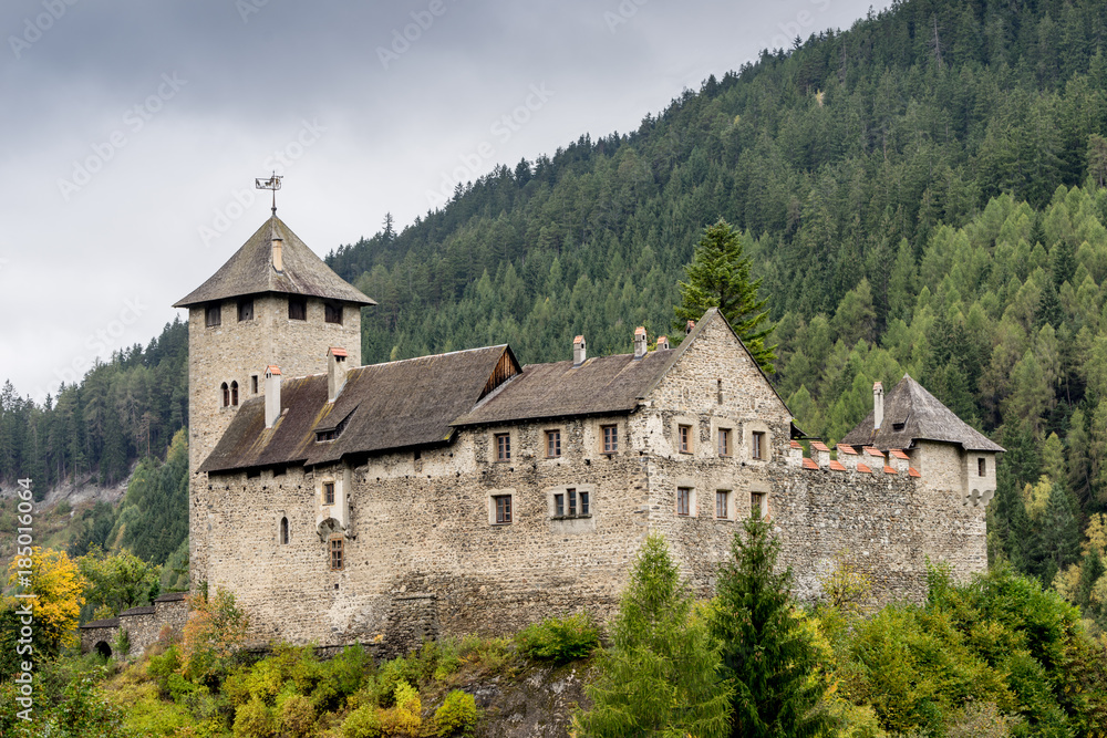 Schloss Wiesberg Castle with bridge over the Trisanna river. Mountain, colored hills and trees landscape natural environment on background. Paznautal Valley, Paznaun, Tyrol, Austria.