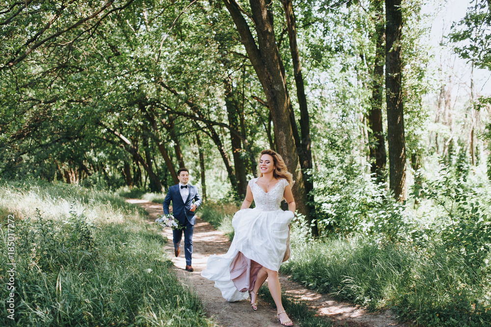 The bride and groom are happily running along the path in the forest. The bridegroom is catching up with the bride. The newlyweds laugh. The bride and groom are happily running along the path in the forest. The bridegroom is catching up with the bride. The newlyweds laugh.