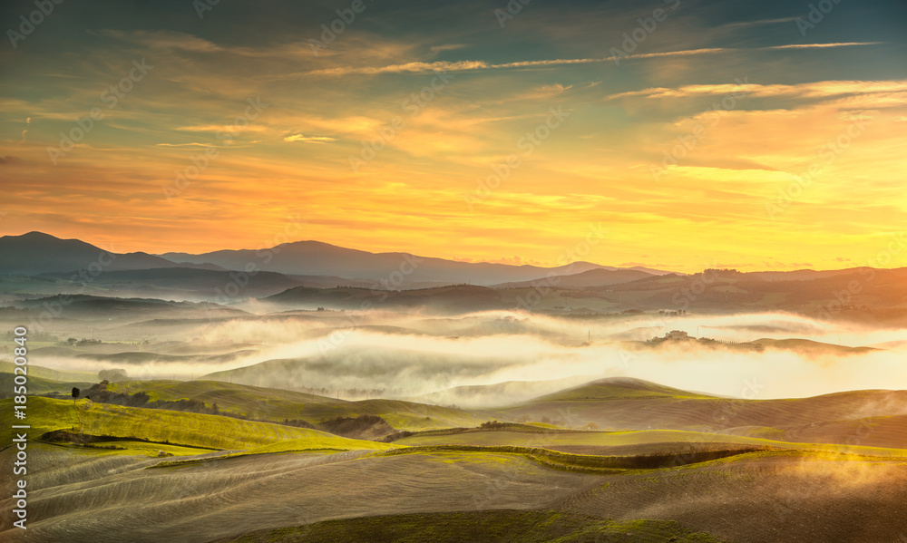 Volterra foggy panorama, rolling hills and green fields on sunset. Tuscany, Italy