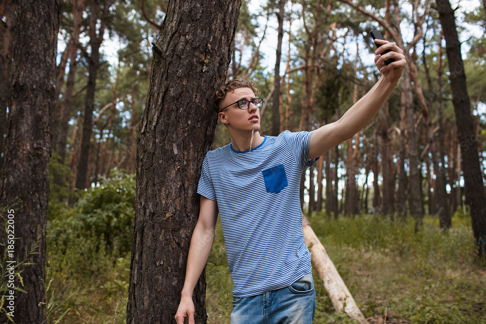 Self-confident man does selfie by the phone in the forest. Alone on the nature. Traveler lifestyle. Self-confident man does selfie by the phone in the forest. Alone on the nature. Traveler lifestyle.