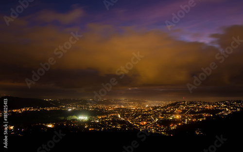 View of Bath at night from Solsbury Hill. The UNESCO World Heritage city seen nestling among hills from a high viewpoint, under low clouds