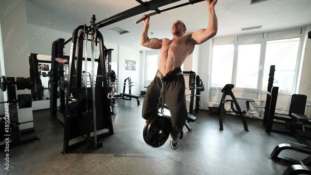 Athlete does pull-up on the crossbar, on his belt an additional load. Athlete does pull-up on the crossbar, on his belt an additional load.