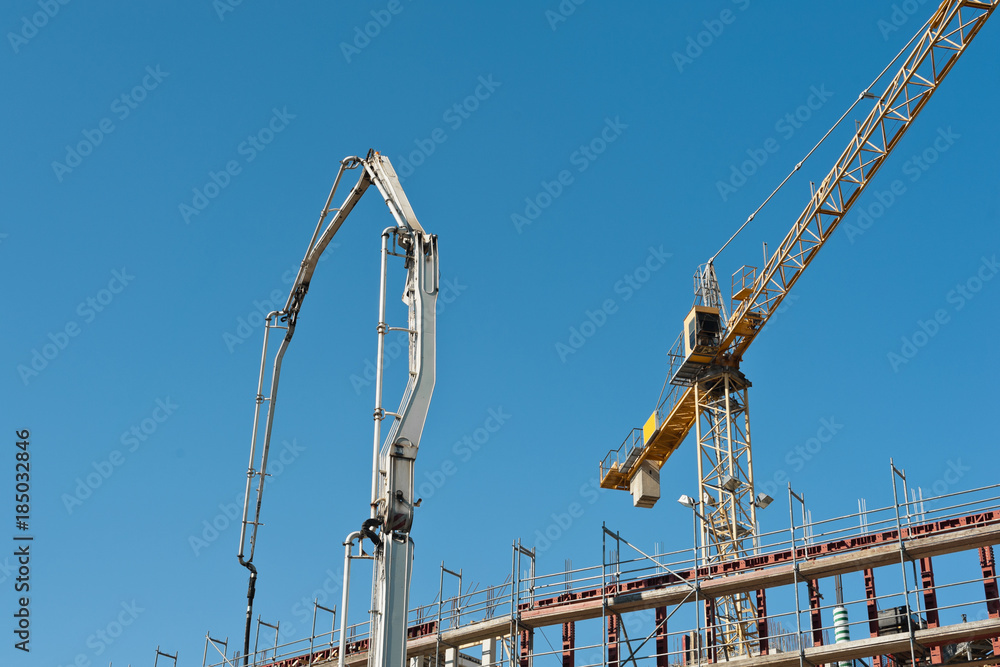 Ein Kran und eine Betonpumpe arbeiten an einem Neubau unter blauem Himmel Ein Kran und eine Betonpumpe arbeiten an einem Neubau unter blauem Himmel