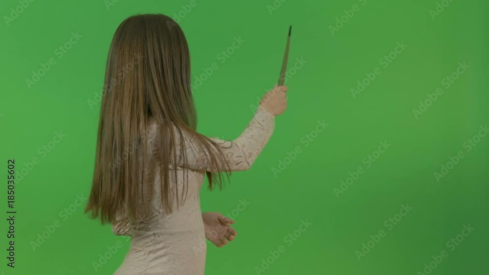 A young girl in a beige dress asks a question and points at the object behind her back. On the green screen. A young girl in a beige dress asks a question and points at the object behind her back. On the green screen.