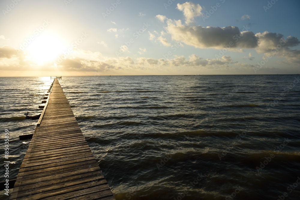 Long wooden pier over water leading to the sunrise and horizon on the Gulf of Mexico