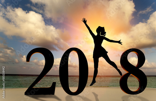 Happy new year card 2018. Silhouette of young woman on the beach stand as a part of the Number 2018 sign with sunset background.