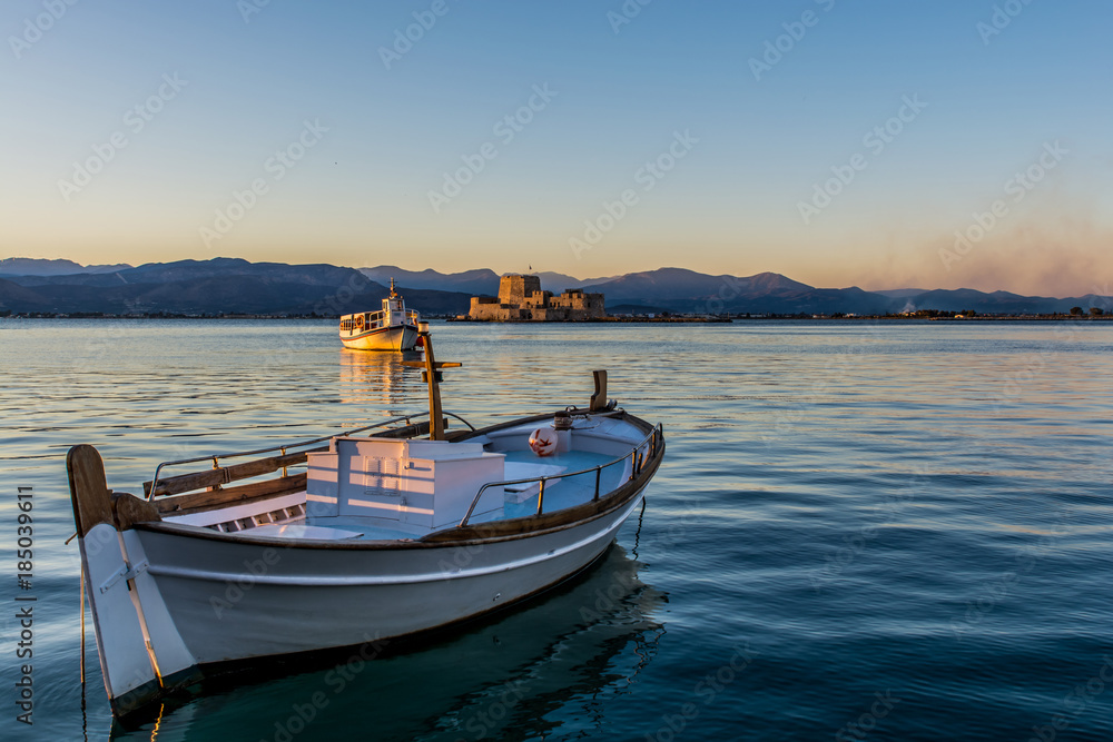A small wooden boat in Nafplio, Greece with Bourtzi view on the background at sunset