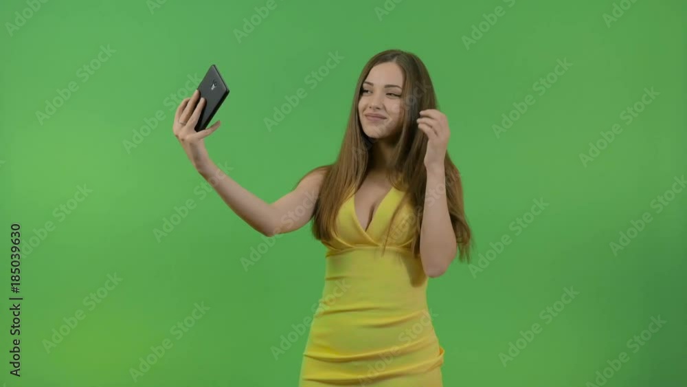 Beautiful young girl in a yellow dress, on a green screen. She takes pictures of herself on a smartphone. Beautiful young girl in a yellow dress, on a green screen. She takes pictures of herself on a smartphone.