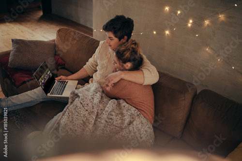 Cozy young couple sitting on sofa with laptop