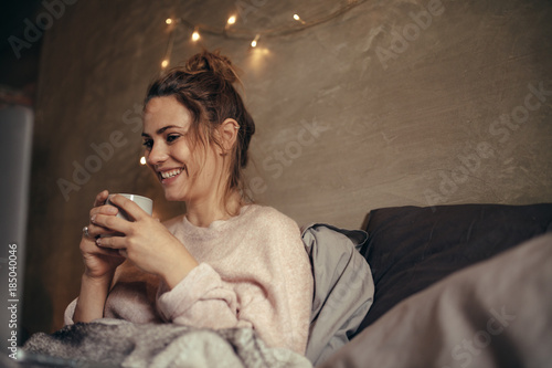 Cheerful woman drinking coffee in bedroom