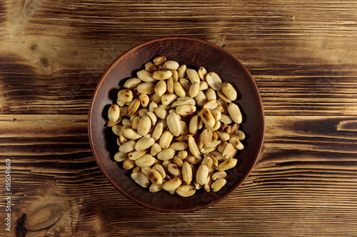 Roasted salted peanuts in plate on wooden table