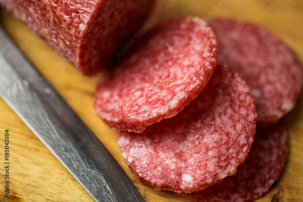 Salami on wooden cutting board with knife, macro photo. Slices of sausage, top view, close up Salami on wooden cutting board with knife, macro photo. Slices of sausage, top view, close up