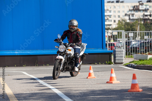 Woman L-driver driving slalom through the cones on training ground on motorcycle