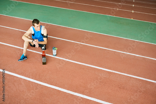 High angle portrait of young amputee athlete sitting on running track taking break from practice to relax, copy space