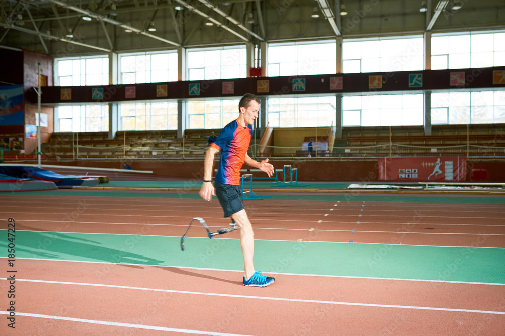 Side view portrait of amputee athlete running on track of  indoor stadium preparing for Paralympic championship, copy space