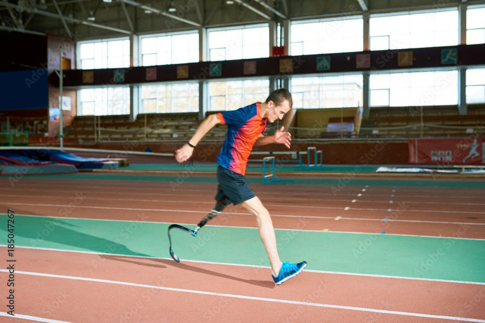 Full length portrait of amputee athlete running on track of  indoor stadium preparing for Paralympic championship, copy space