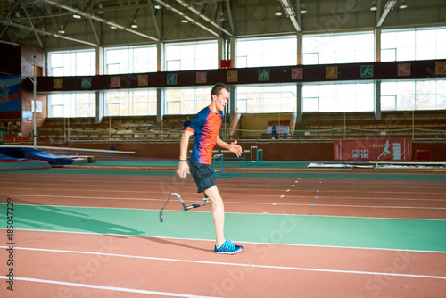 Side view portrait of amputee athlete running on track of  indoor stadium preparing for Paralympic championship, copy space © Seventyfour