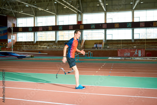 Side view portrait of amputee athlete running on track of indoor stadium preparing for Paralympic championship, copy space