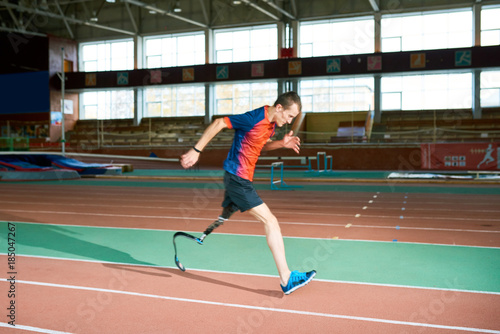 Full length portrait of amputee athlete running on track of indoor stadium preparing for Paralympic championship, copy space