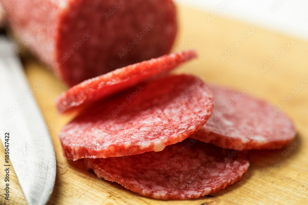 Salami on wooden cutting board with knife, macro photo. Slices of sausage close up