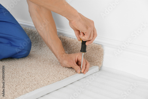 Worker using screwdriver while installing new carpet flooring in room