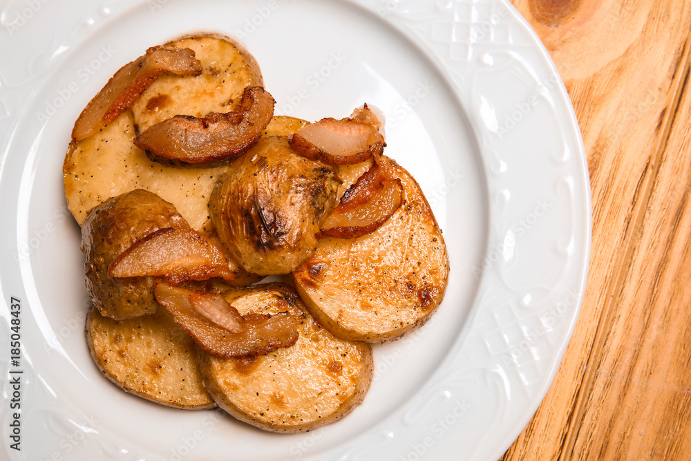 Plate with tasty fried potato and bacon crisps on wooden table, closeup Plate with tasty fried potato and bacon crisps on wooden table, closeup
