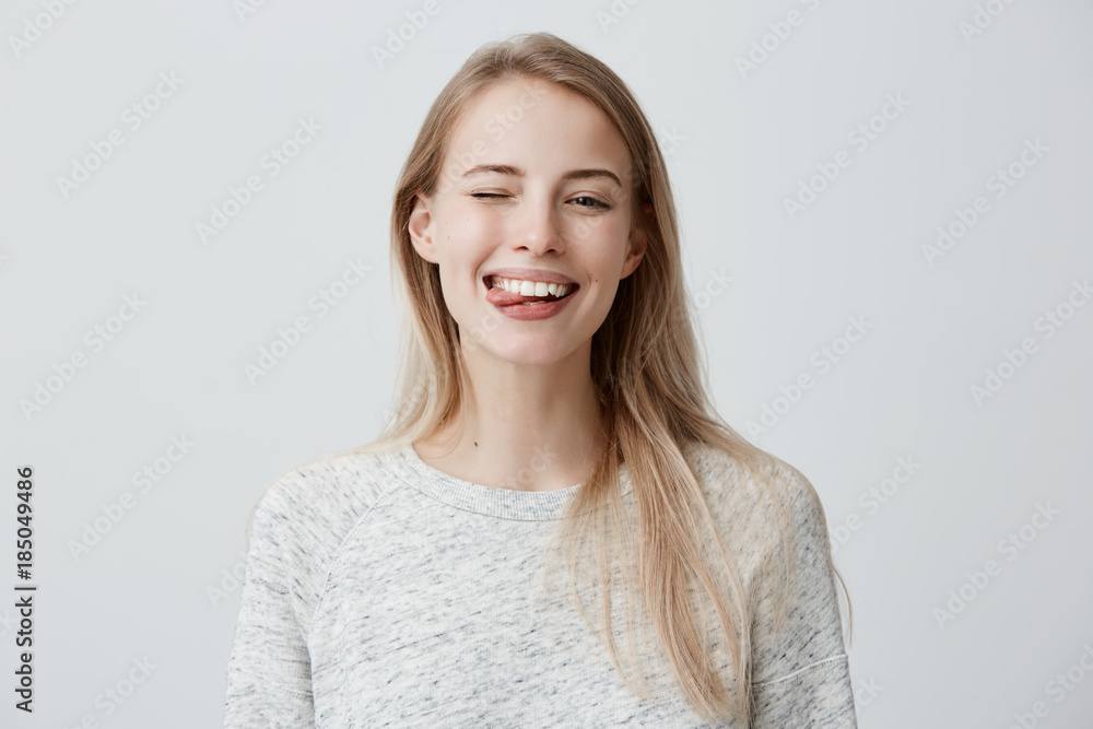 Gloomy young blonde woman with dyed hair dressed casually making faces at camera, blinking, sticking out her tongue. Positive girl having fun indoors Gloomy young blonde woman with dyed hair dressed casually making faces at camera, blinking, sticking out her tongue. Positive girl having fun indoors