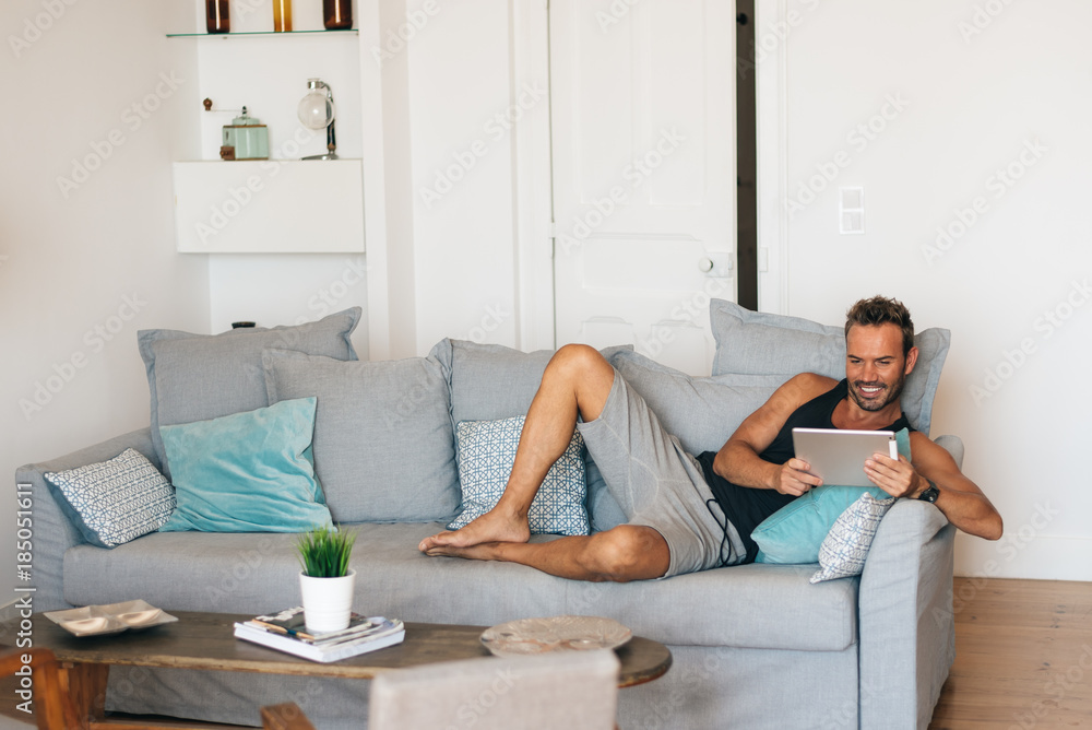 Happy young blonde man sitting in the couch at home on the tablet . Happy young blonde man sitting in the couch at home on the tablet .