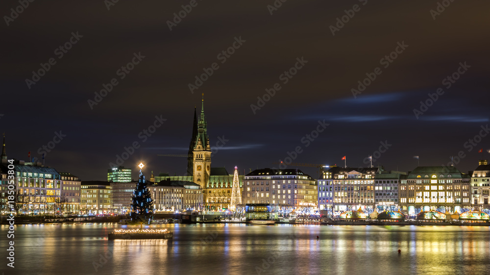 Christmas in Hamburg. Panoramic view of the decorated city center from Alster Lake, view to Hamburg Rathaus and a christmas tree installed in the center of the lake. Atmosphere before the New Year. 