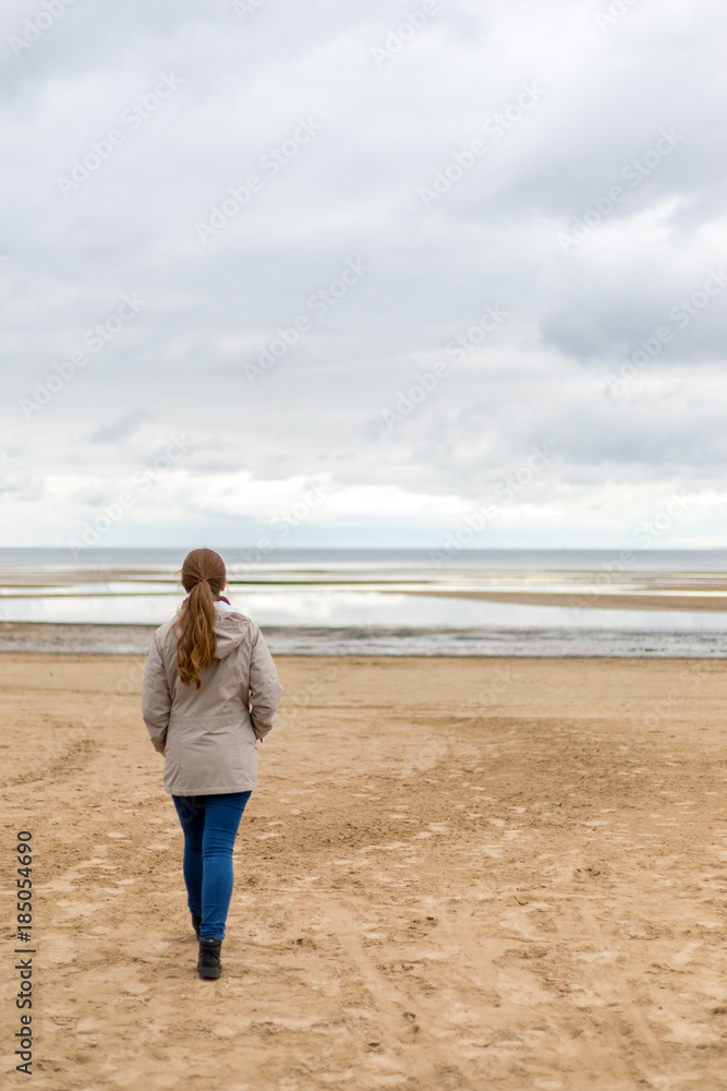 Woman on the beach looks on the sea waves