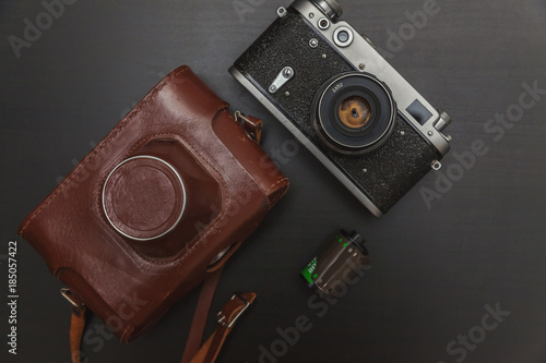 Vintage Film Camera And Roll On Black Wooden Background Technology Development Photographer Concept. Top View