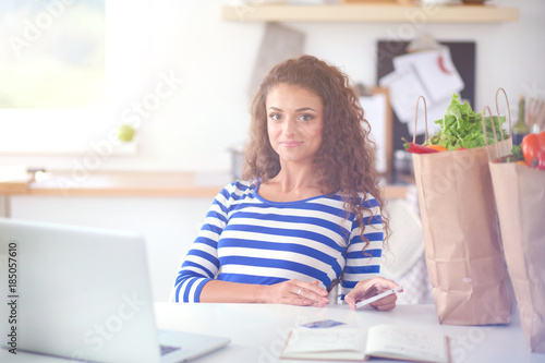 Smiling young woman with coffee cup and laptop in the kitchen at home. Smiling young woman