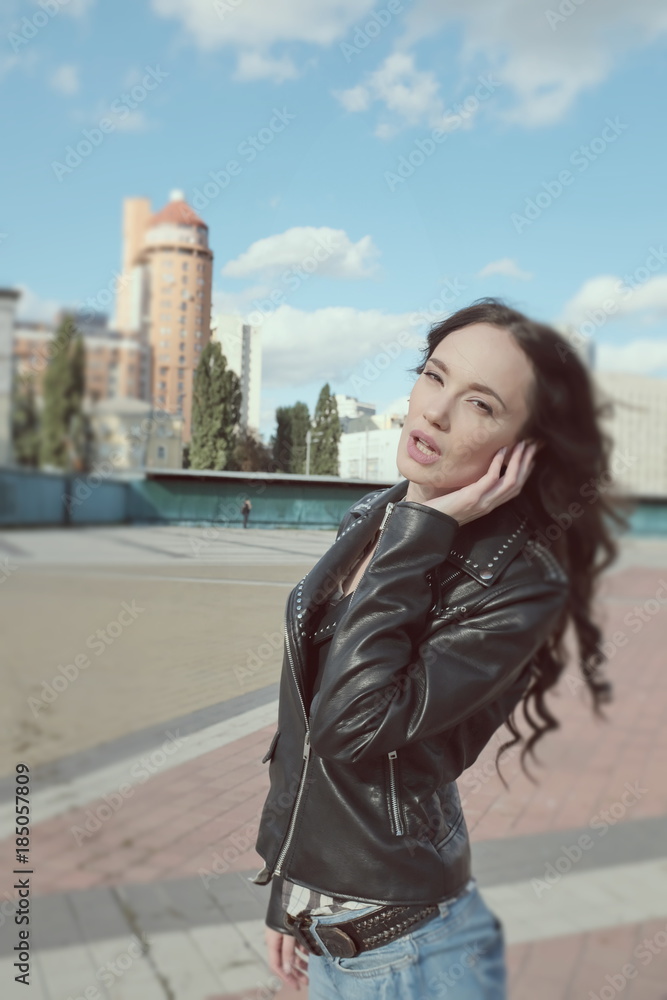 Fototapeta premium Sexy beautiful girl in leather jacket poses in a city center
