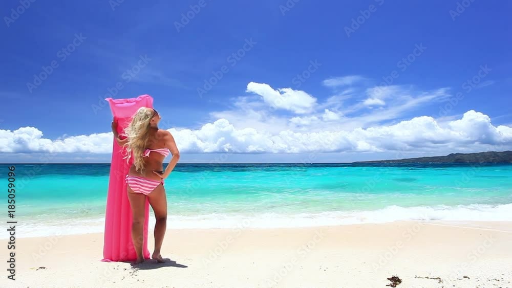 Blond woman with pink swimming mattress on sandy beach. Tropical vacations Blond woman with pink swimming mattress on sandy beach. Tropical vacations
